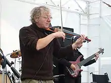 white male standing onstage with another musician, playing a violin