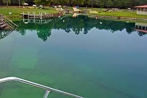 A pond with bluish-green water, several buoys and recreational facilities around it, seen on a cloudy day