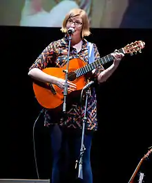 Photograph of Laser playing a guitar and singing into a microphone.