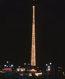 A nighttime photograph featuring a tall, thin tower festooned with lights