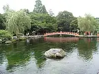 Pond with a stone inside and a red bridge crossing it.