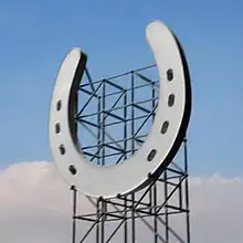 A digital image of a giant horseshoe suspended on the front of metal scaffolding.