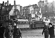 Intersection of Marszałkowska Street and Aleje Jerozolimskie (Jerusalem Avenue) in Warsaw during German occupation. Visible tramway #3 with a billboard "Kamea woda kwiatowa". Behind it ruins of destroyed in 1939 townhouse at Marszałkowska 98/al. Jerozolimskie 33 streets.