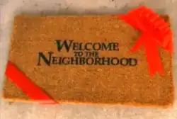 A title card for the American television series Welcome to the Neighborhood, featuring black letters on brown doormat that has a red ribbon wrapped around two of its ends