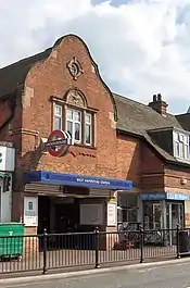 A brown-bricked building with a rectangular, dark blue sign reading "WEST HAMPSTEAD STATION" in white letters all under a blue sky