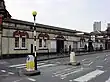 A dirty, white-bricked building with a rectangular, dark blue sign reading "WESTBOURNE PARK STATION" in white letters all under a blue sky