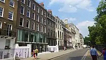 urban streetscape with trees and grassed area to one side and terraced 18th century buildings on the other