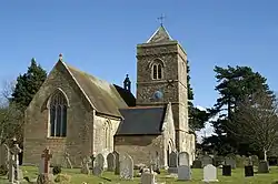 Stone building with arched windows and square tower. In the foreground is a grass area with gravestones.