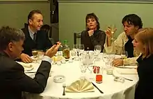 five of the main actors sitting around a dinner table