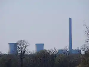 Two cooling towers and one smoke stack, with white aviation lights, as seen towering over the trees in the foreground.