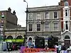 Two entrances on the ground floor of what looks like a terraced house between a shop with green sign reading "Fresh" and a building with a sign reading "Lecture Hall" above a door