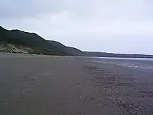 Photograph of the wide sandy beach with hills behind it