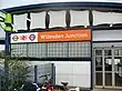 A white-panelled building with a rectangular, orange sign reading "Willesdon Junction" in white letters all under a light blue sky