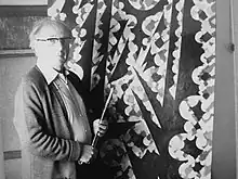 Black and white photograph of Gear in front of a painting at his Edgbaston Studio. Taken August 1979