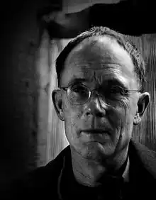 Head shot of a short haired man wearing rimless glasses. His eyes are in shadow.