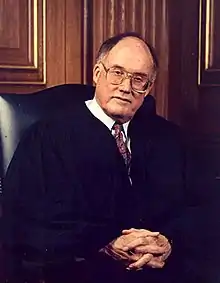 Photograph of a balding white male sitting, in judicial robes