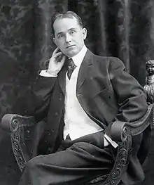 A black and white photograph of a middle-aged man in a suit posing reclined in a chair