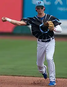 A man in a black baseball jersey, white pants, and blue cap