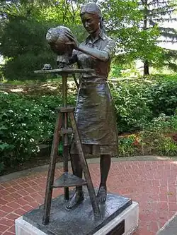 A statue of a standing woman sculpting a face.