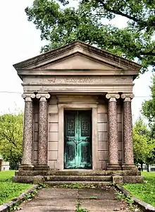 Stone mausoleum with four Ionic columns, an oxidized copper or bronze door and sign SAVERY above.