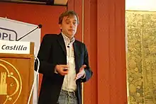 A man talking and gesturing while holding a projector remote