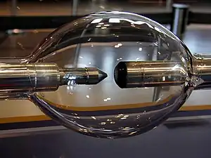 Elongated glass sphere with two metal rod electrodes inside, facing each other. One electrode is blunt and another is sharpened.