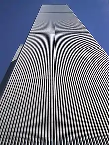 Aerial view of two 110-story twin towers; the building have gray, steel exteriors, and the structure on the left is topped by a large antenna. Several skyscrapers are visible surrounding the two towers.