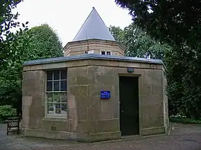 Small five-side stone building. The only floor contains a door and window and is topped by a short, pointed tower.