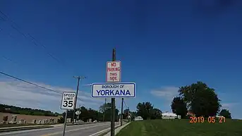 A simple white sign with blue text reading "Borough of Yorkana" on the side of the main road.