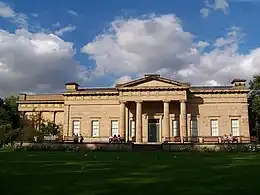 Stone block building with columned portico and large wing extending behind.