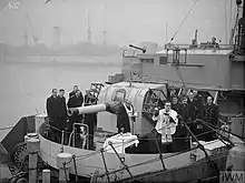 a black and white photograph of the main gun of ship with a group of men around it