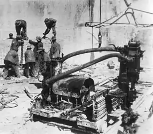 Channeling machine (a series of drills) for making vertical holes in marble. Background-block being rigged for lifting out of the quarry.