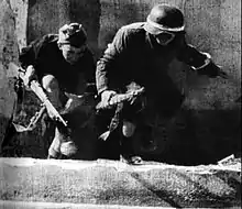 The film still shows two young boys dressed in captured German military uniforms, with Polish national colours marked on the helmet of one of them, armed with bolt action rifles, passing a street under enemy fire during the Warsaw Uprising.