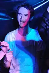 Zedd in a white T-shirt, looking to his right and smiling