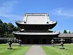 Wooden building with a metal plate covered roof and an enclosing pent roof giving it the appearance of a two-storied structure.