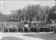 Black and white photograph of people gathered around the statue. Healy Hall is in the background; its entrance is draped in patriotic bunting