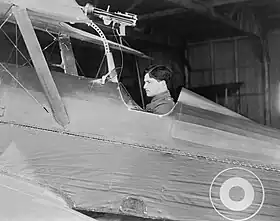 Side view of dark-haired man in open cockpit of biplane equipped with machine-gun on upper wing