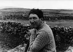 Black and white photograph of farmer John Conneely working in a field on Inis Mor in the Aran Islands. The farmer looks to camera while he leans on a shovel