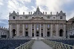 Ornate building in the early morning with a giant order of columns beneath a Latin inscription, fourteen statues on the roofline, and large dome on top.