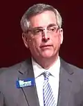 Brad Raffensperger wearing a grey suit with a name tag.