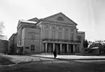 A grayscale image of a small museum with a statue of two men in front.