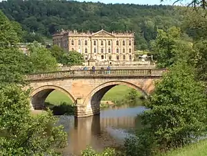 Large country house by river with wooded hillside beyond