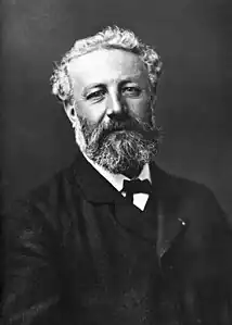 Black and white photo of man in formal dress with unkempt hair, moustache and beard.