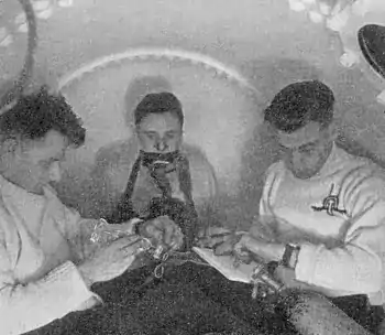 Three men inside a pressure chamber. One is breathing from a mask and the other two are timing and taking notes.