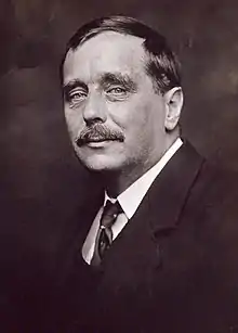 Black and white photo of a man with bushy black moustache and black hair with parting.