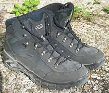 Two dark gray ankle-covering boots covered in suede and cloth with laces going through hooks rather than eyelets, on a pebbly surface