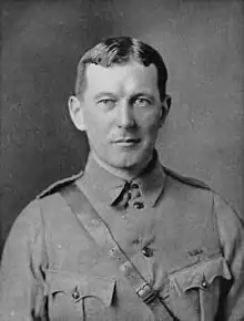 Upper body of a man in a soldier's uniform. He has short dark hair parted in the middle and maintains a neutral expression.