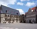 A town square with two visible buildings and a few tourists.