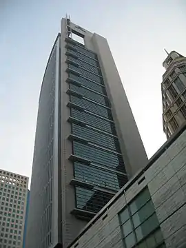 Ground-level view of a 30-storey building with a rounded, glass facade on one side and a straight-edged facade of concrete and windows on another; the concrete siding protrudes above the roofline