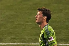 A grown Caucasian man in a light green shirt stares to the camera's left against a green background